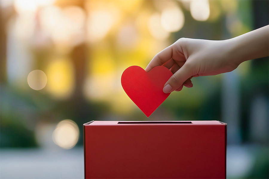 Hand, die ein Herz aus Papier in eine Spendenbox gibt