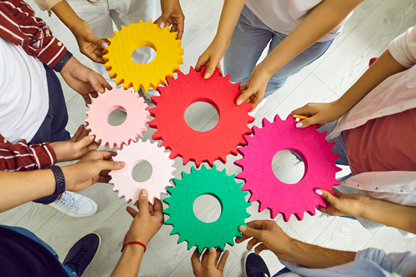 Mehrere Hände, die bunte Schaumstoff-Zahnräder zusammenhalten