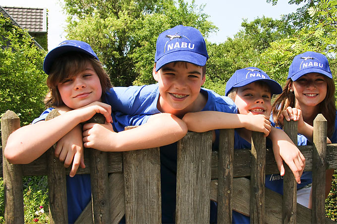 Kinder in NABU-Kleidung lehnen über einen Zaun